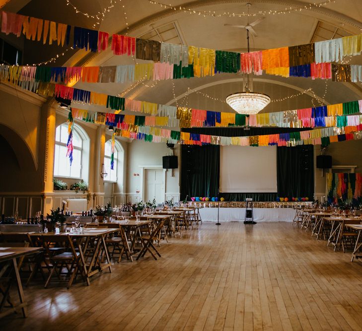 DIY Village hall wedding with wooden tables and colourful Streamers hanging from the ceiling 