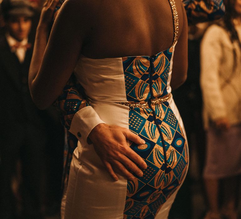 Groom putting his hand on his brides bottom in a white fitted dress with blue and gold West African tribal print 