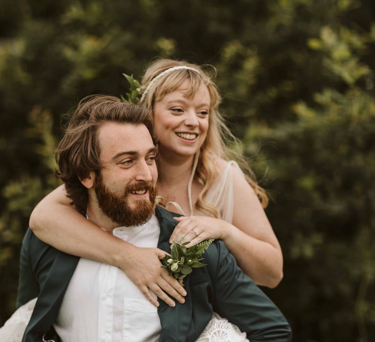 Groom carries bride in a piggy back during botanical wedding