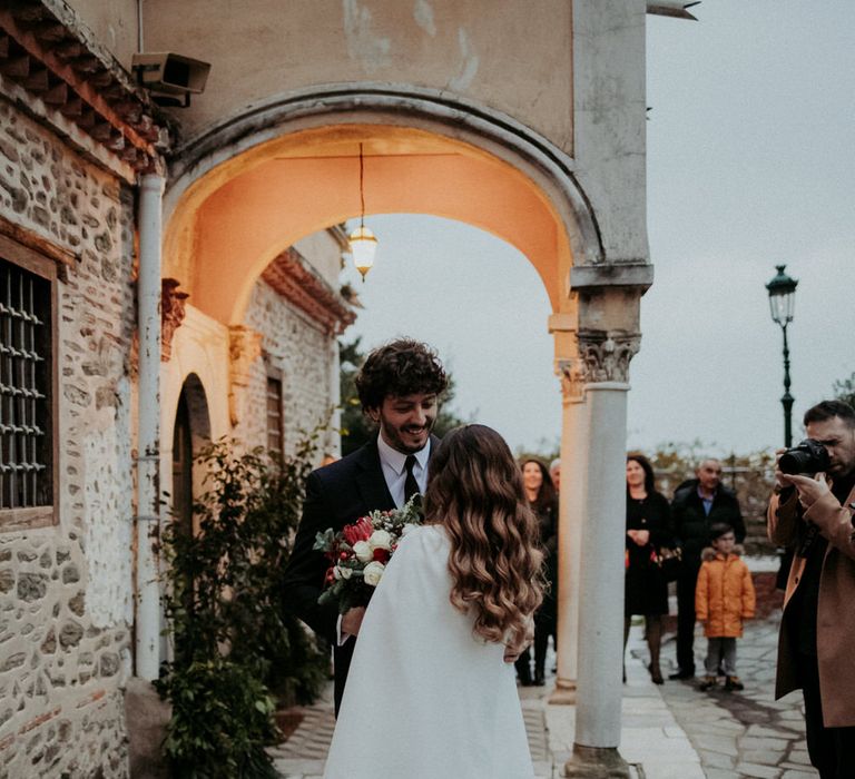 The bride and groom outside their church wedding ceremony, the bride is wearing a long white bridal cape