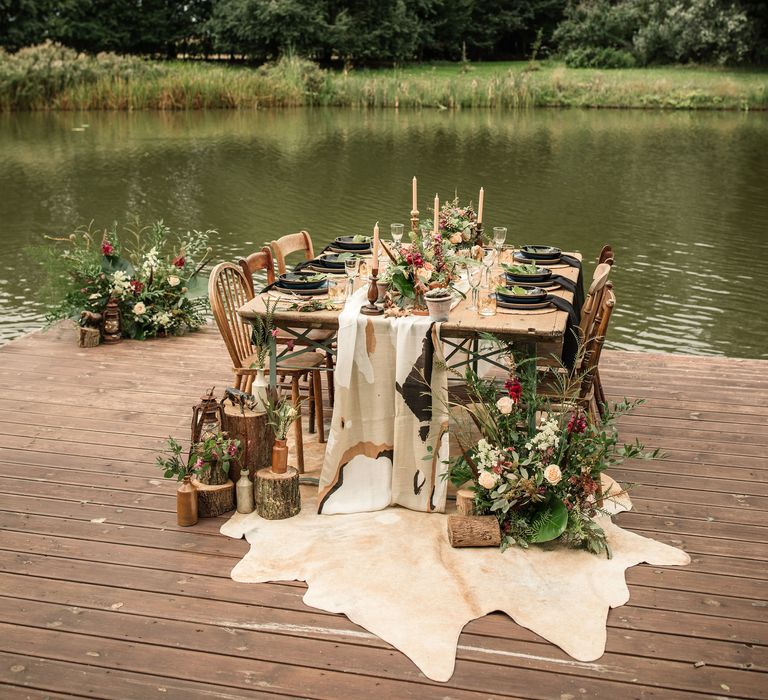 Wooden table sits on dock in front of lake with camouflage table runner