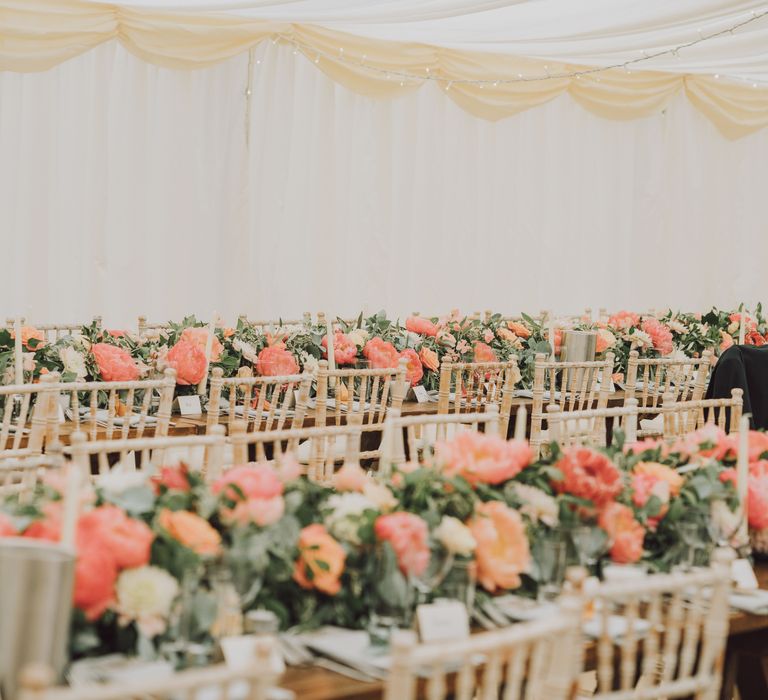 Wedding marquee featuring peach florals and green foliage bouquets lining each table