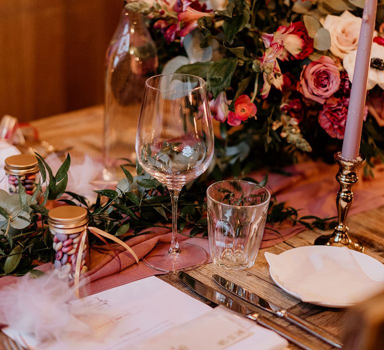 Table setting with pink floral decor and wedding favours on wooden table