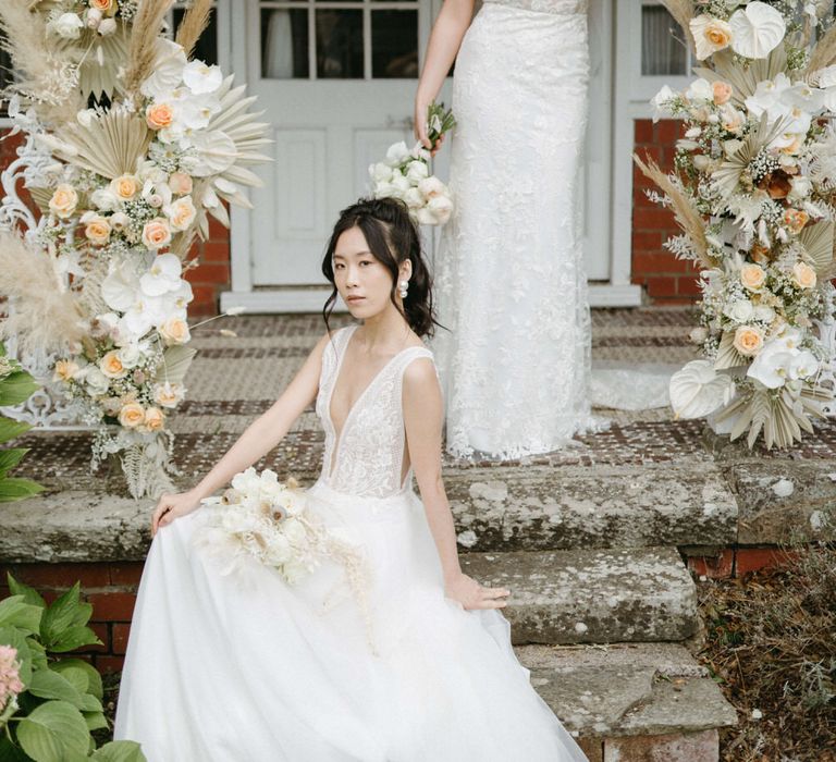 Two brides at Berwick lodge under boho flower arch, wearing boho inspired plunge neck tulle wedding dresses with floral detail