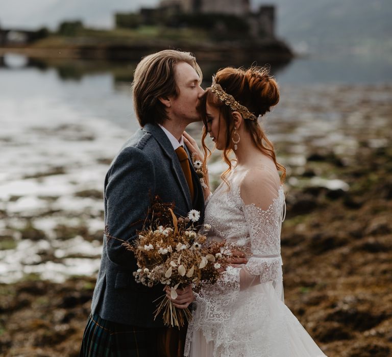 Groom kisses the forehead of bride with Eilean Donan Castle in the background