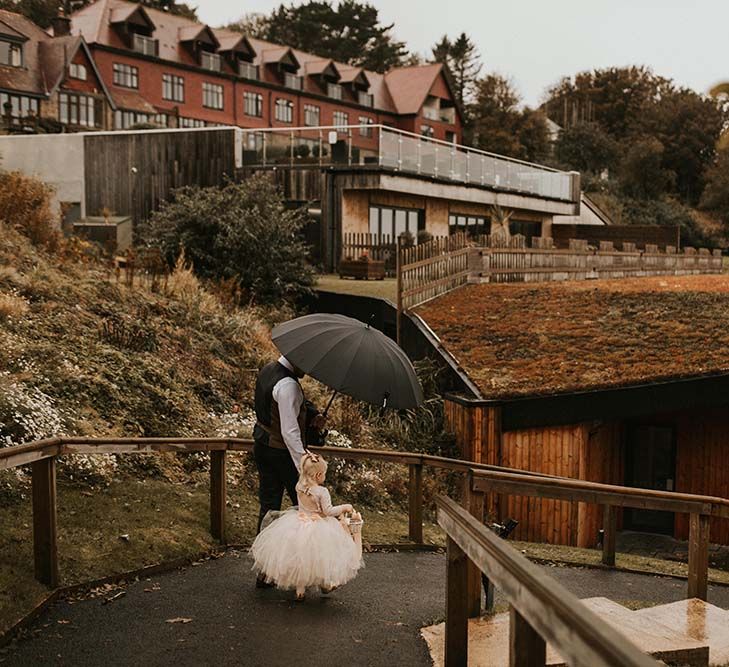 Groom holding an umbrella walking along the path with his daughter in a tutu