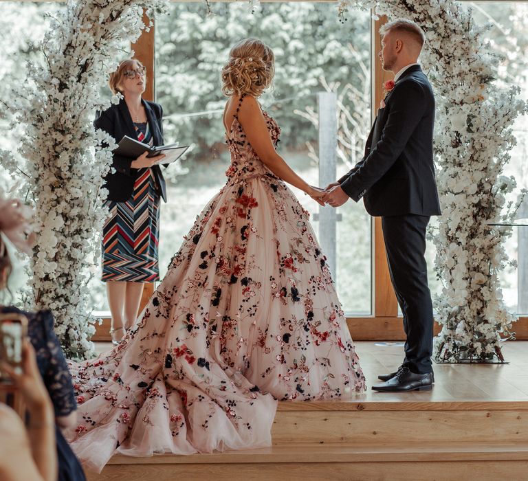 Bride & groom stand beneath floral arch during wedding ceremony