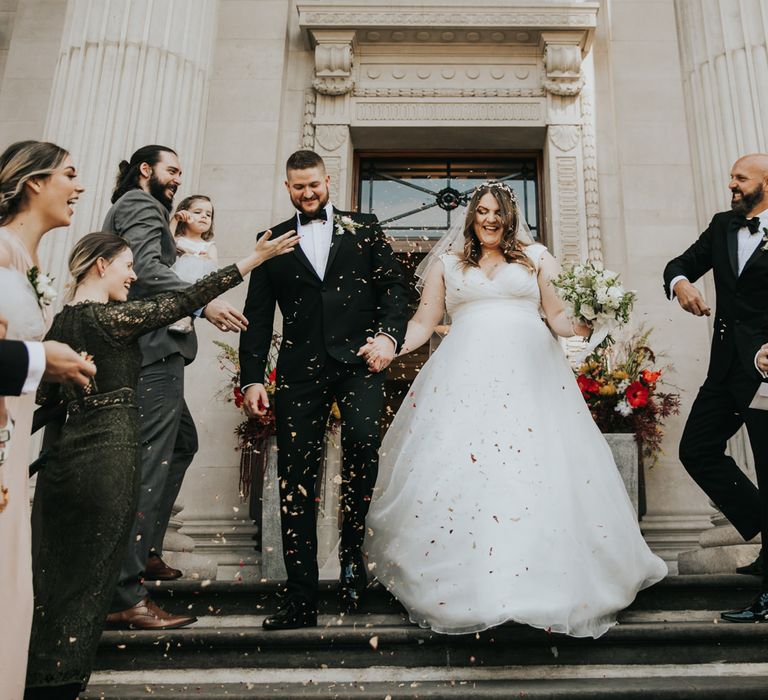 Bride & groom walk down the steps of The Old Marylebone Town Hall whilst confetti is thrown around them