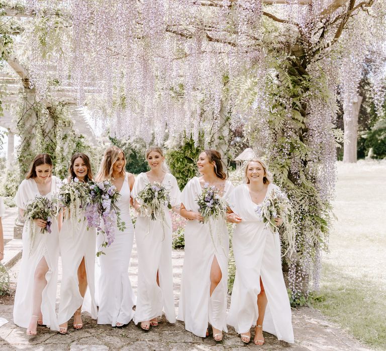 Bride stands with her bridesmaids in white dresses from ASOS all carrying lilac bouquets