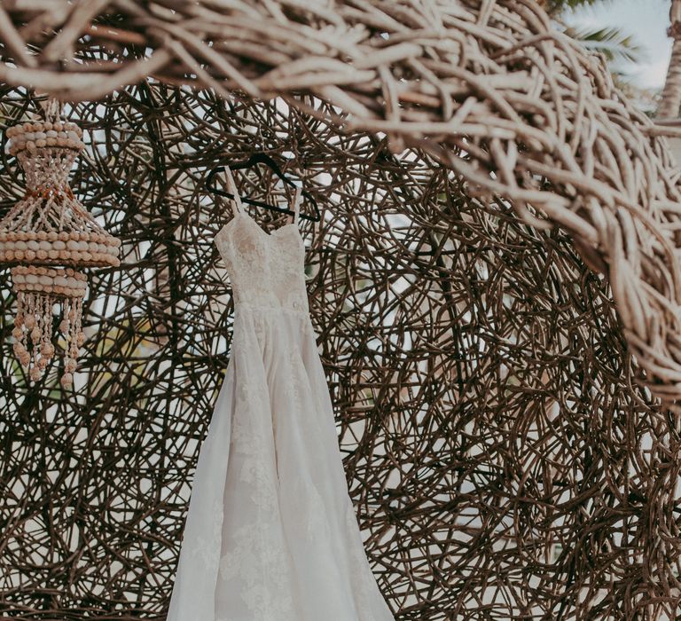 Bridal gown hangs within wooden woven cove on the beach