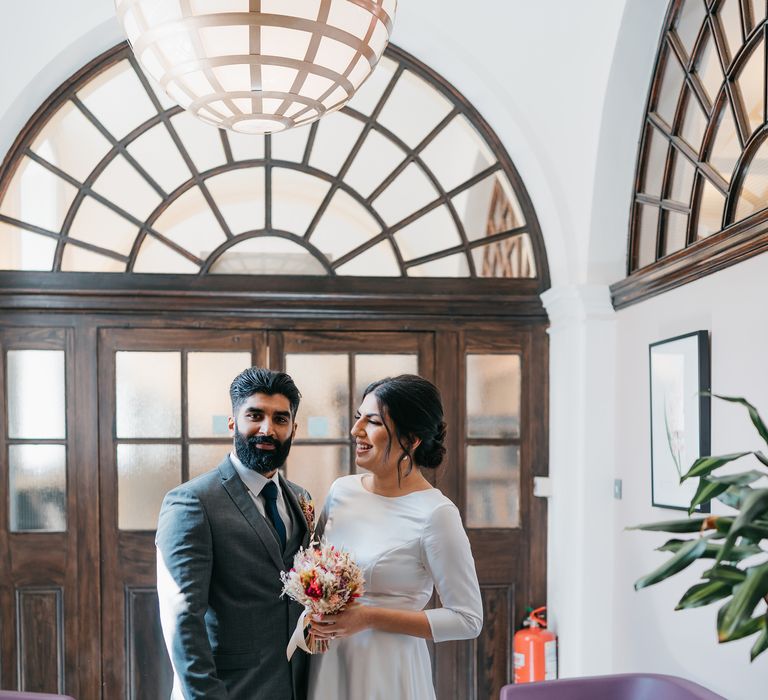 Bride & groom stand with one another within Chelsea Old Town Hall on their wedding day for Civil Ceremony