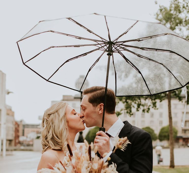 Bride and groom kissing under a clear umbrella at their Leeds city wedding 