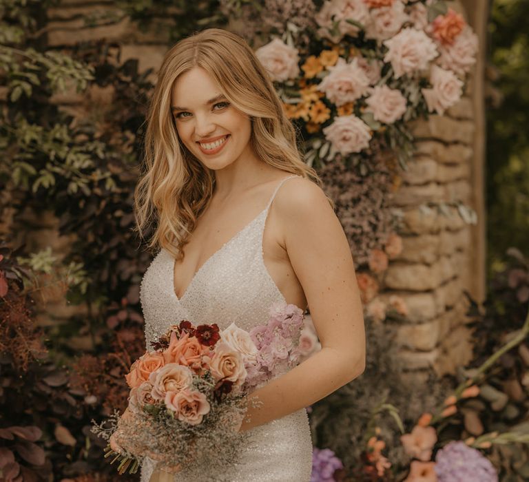 Beautiful bride in a sequin Made With Love strappy dress holding an pastel orange, peach and coral wedding bouquet 