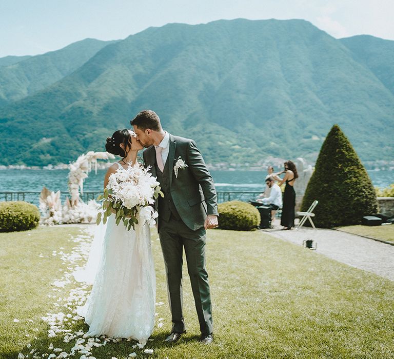 Groom kisses his bride on their wedding day as Lake Como glistens in the sunlight