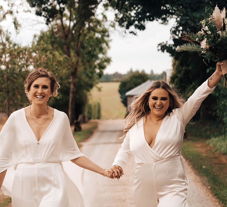 Blonde bride lifts her hand in the air in celebration as she holds hands with her wife on wedding day