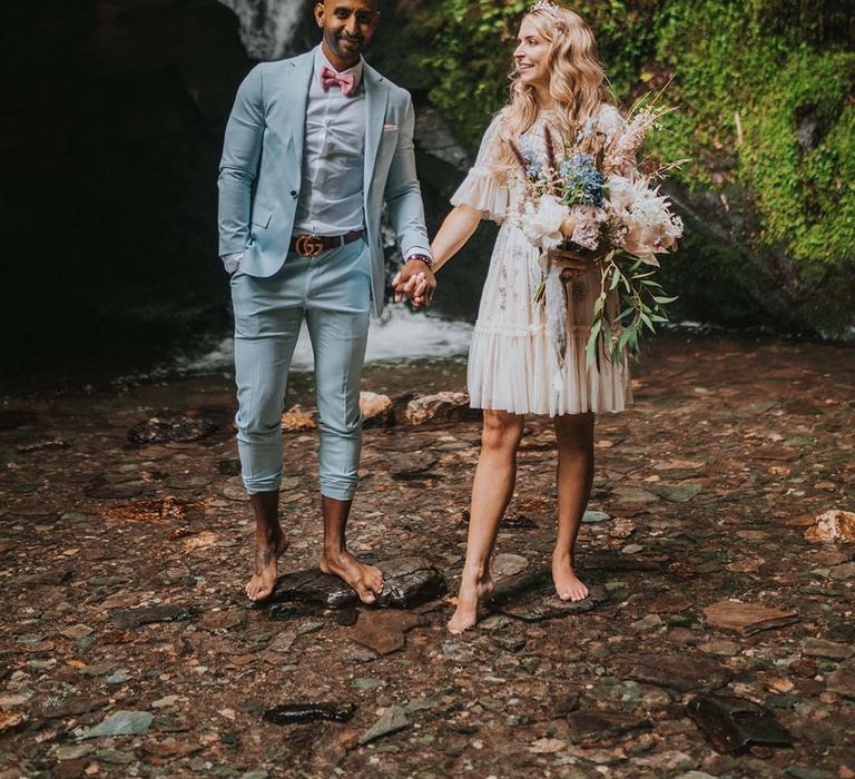 Bride & groom hold hands as bride wears short Needle & Thread wedding gown