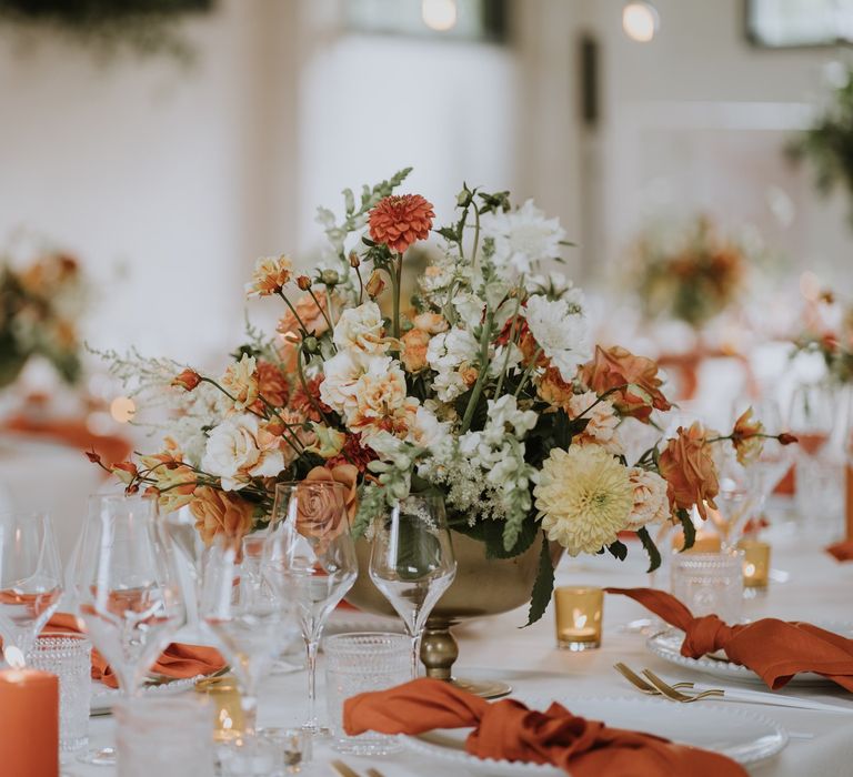 Orange, peach and white floral centrepiece in a gold vessel 