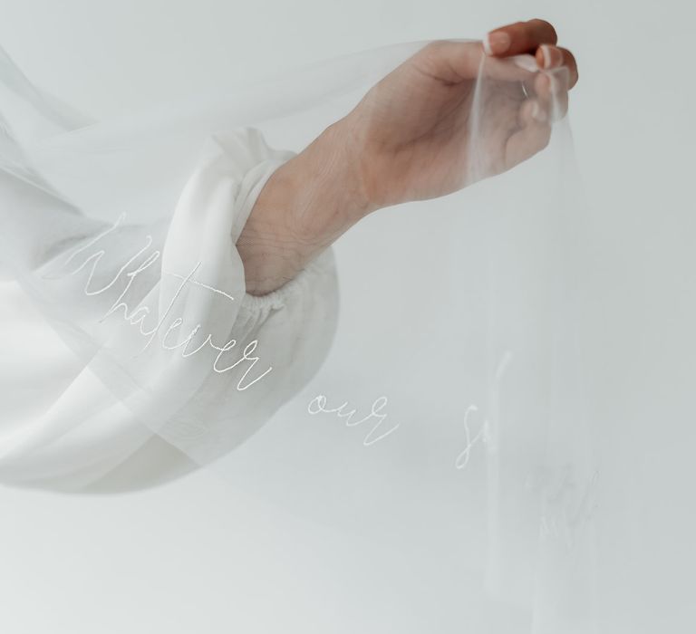 Bride in a long sleeve wedding dress with French manicured nails holding out her embroidered veil 