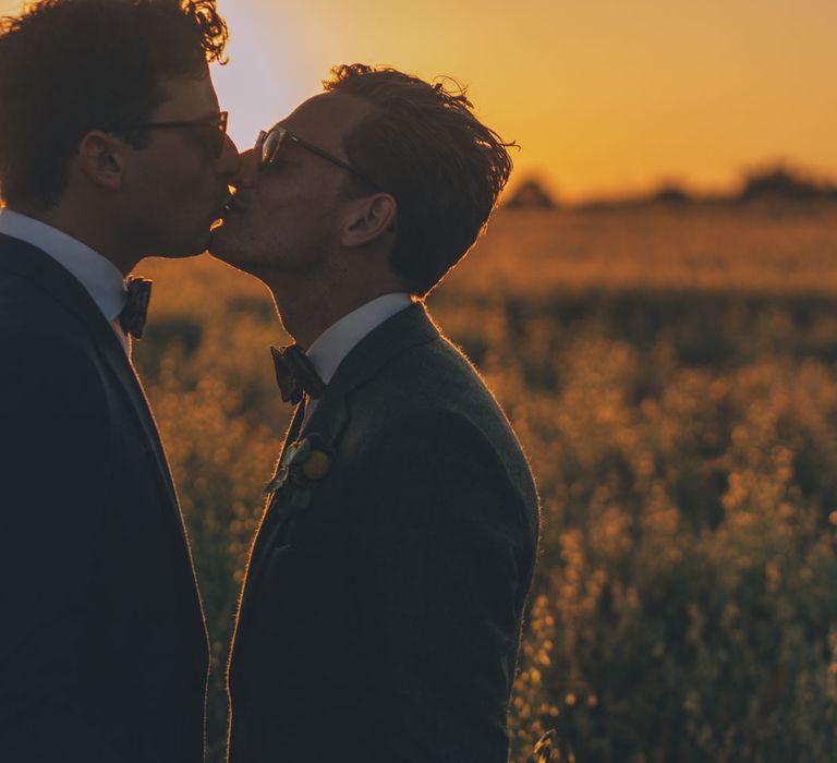 Grooms kiss outdoors in the fields on their wedding day during sunset  | Story + Colour