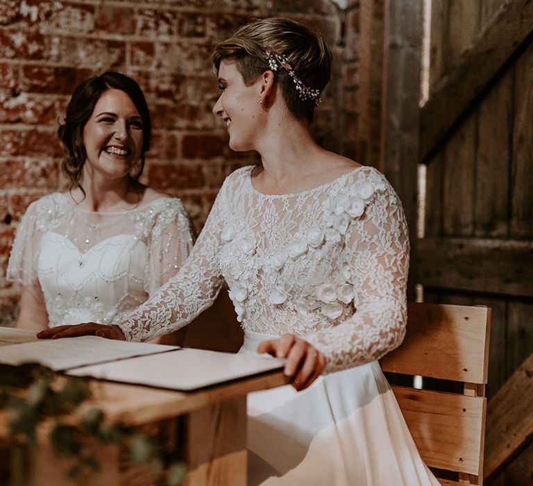 Two brides signing the register at their Woolas Barn wedding wearing an appliqué wedding dress with long sleeves and embellished wedding dress