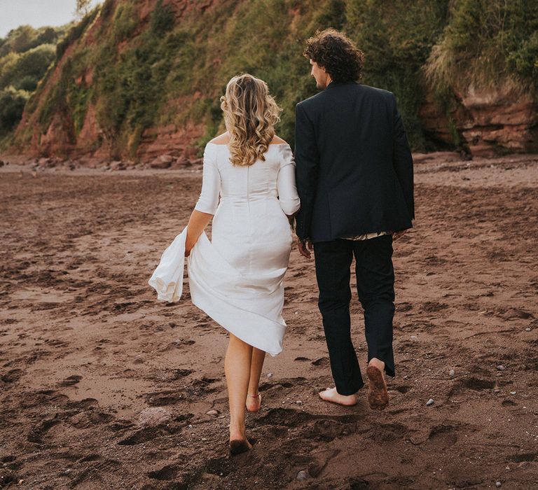 Bride & groom walk along the beach with one another on their wedding day