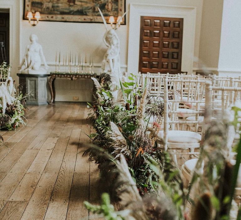 Green foliage lines the aisle at Elmore Court complete with white wooden chairs