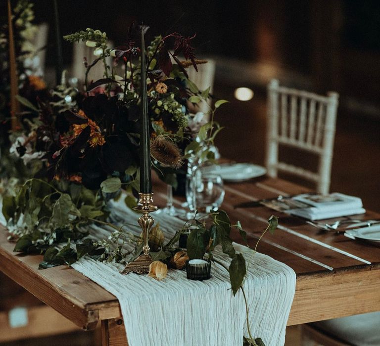 Rustic table complete with crinkled white sheet running down the middle and floral bouquet