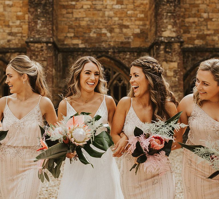 Bride laughs with her bridesmaids as they link arms and walk together outside church