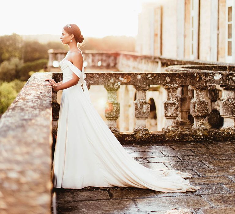 Bride stands on balcony as the sun shines behind her on her wedding day