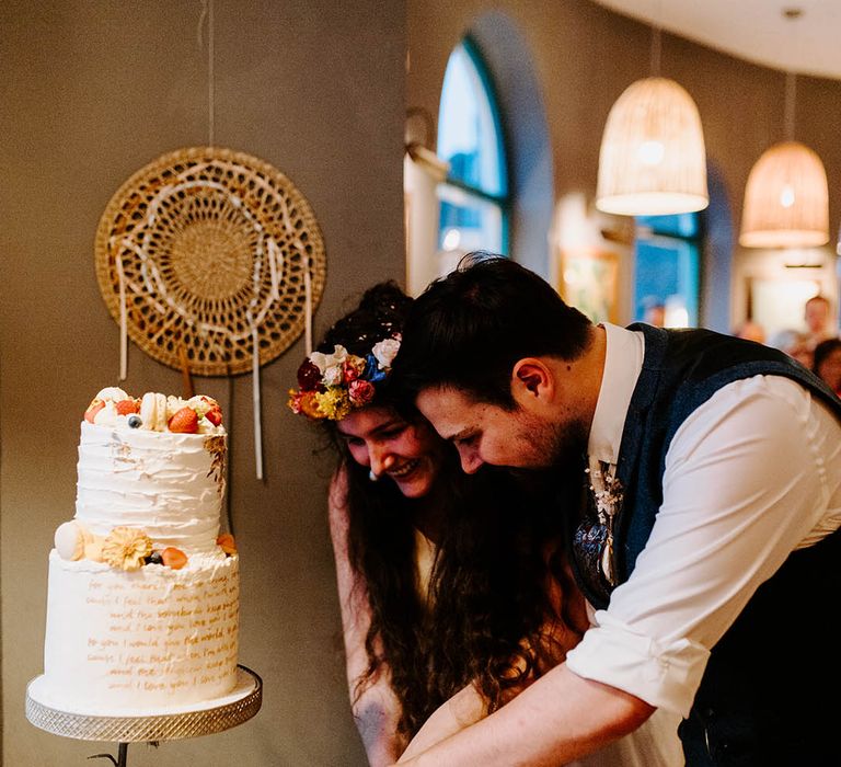 Bride & groom cut their 3-tier wedding cake complete with gold leaf decor and calligraphy 