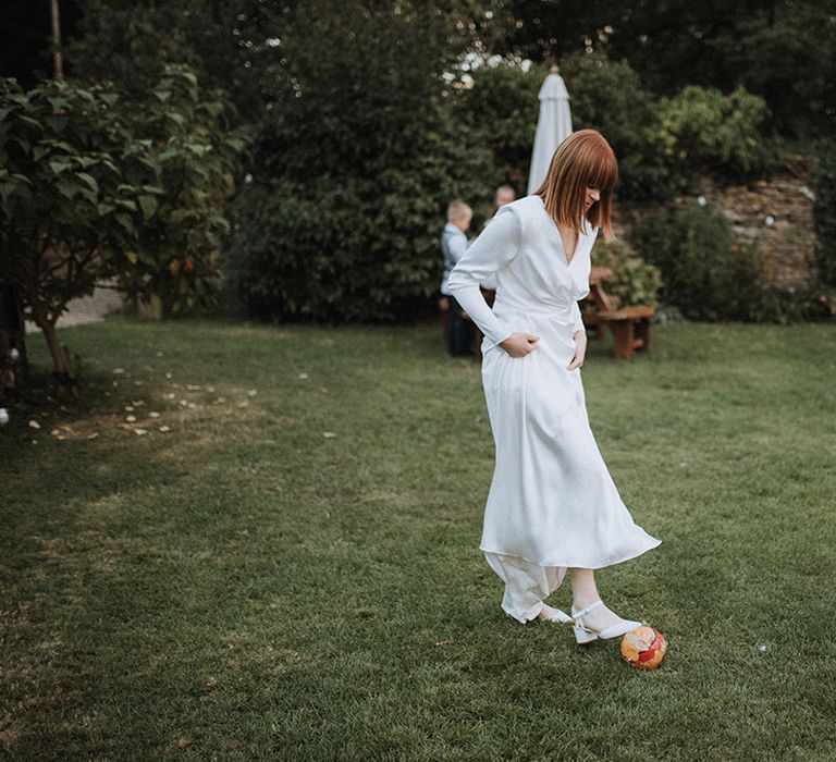 Bride in long sleeve wedding dress plays football at wedding 