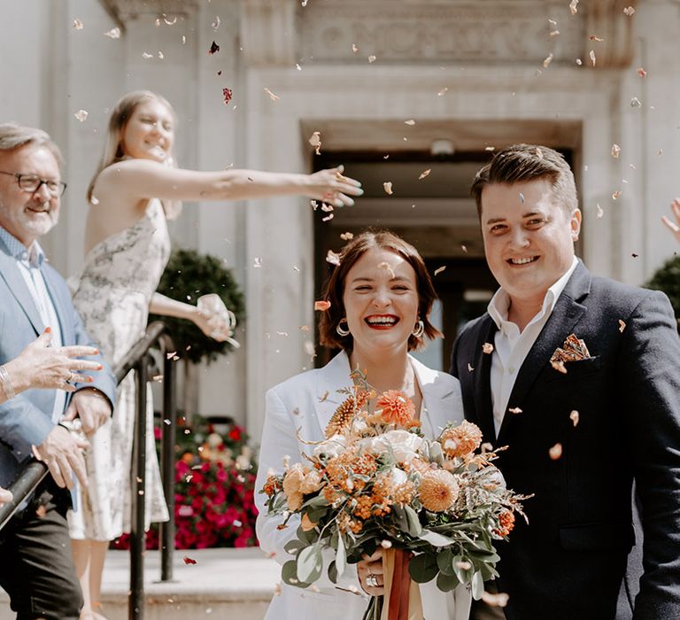 Confetti moment at Town Hall wedding with bride holding an orange flower bouquet 