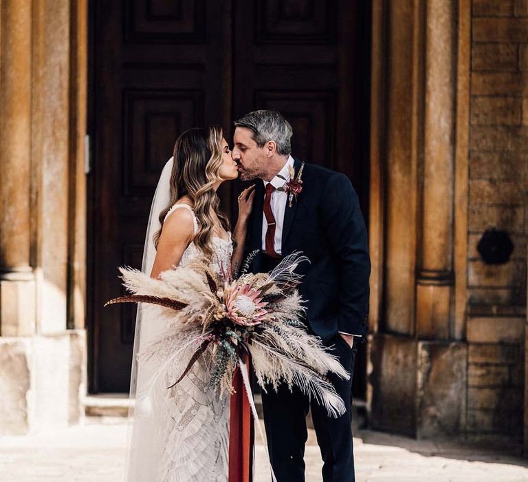 Bride & groom kiss as bride holds statement floral bouquet 