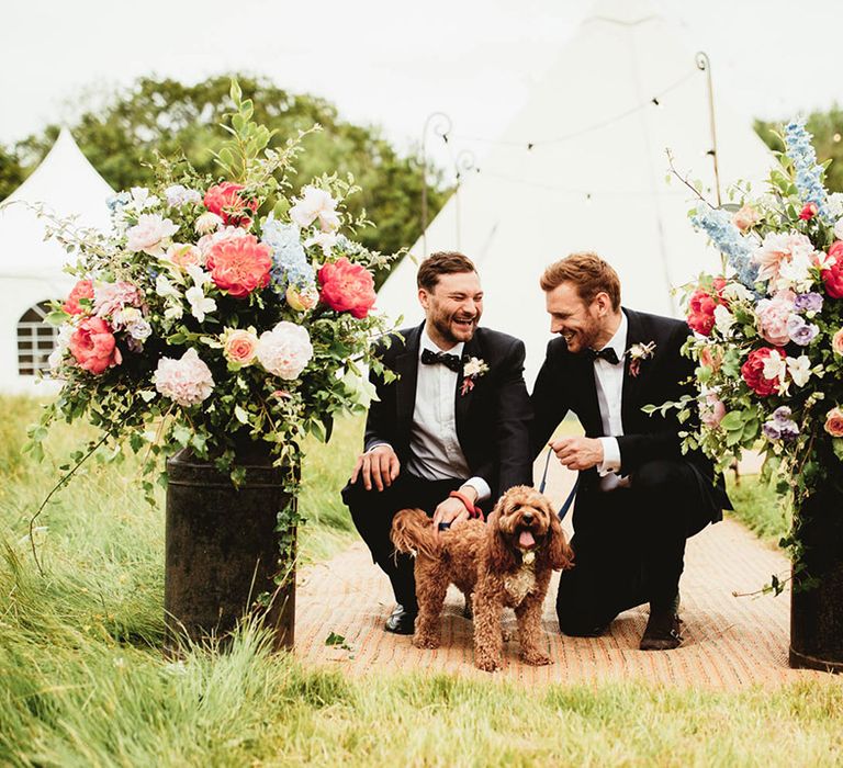 Groomsmen stand with cavapoo on wedding day outdoors