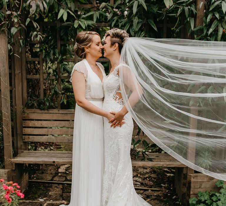 Brides hold hands outdoors as brides veil blows in the wind