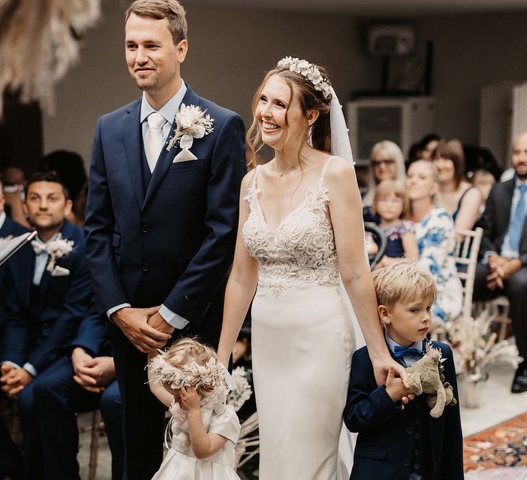 Bride & groom stand together with their daughter and son on their wedding day