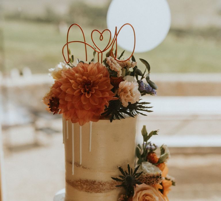 Two tier semi naked wedding cake with drip icing, floral decor and personalised wedding cake topper