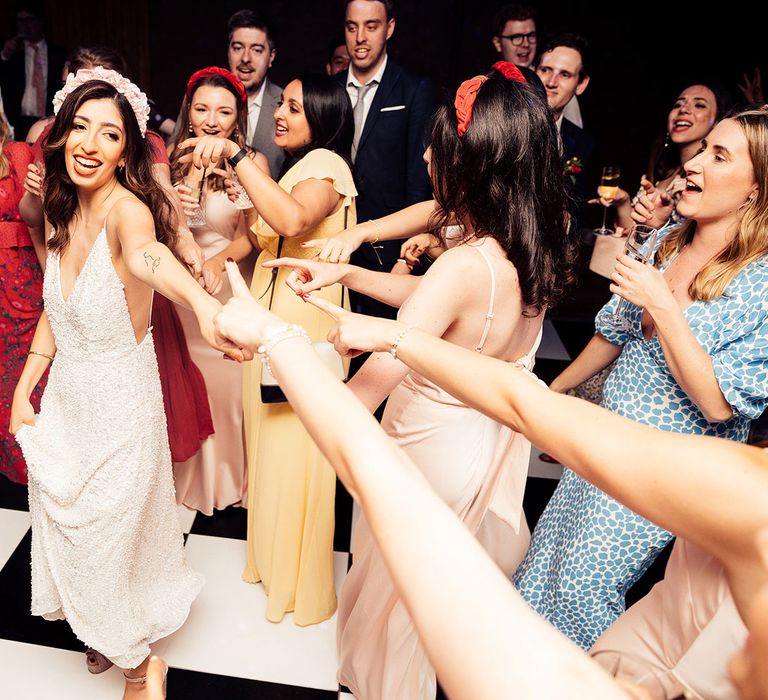 Bride in pink floral headband and white beaded midid dress dances with wedding guests on black and white dancefloor