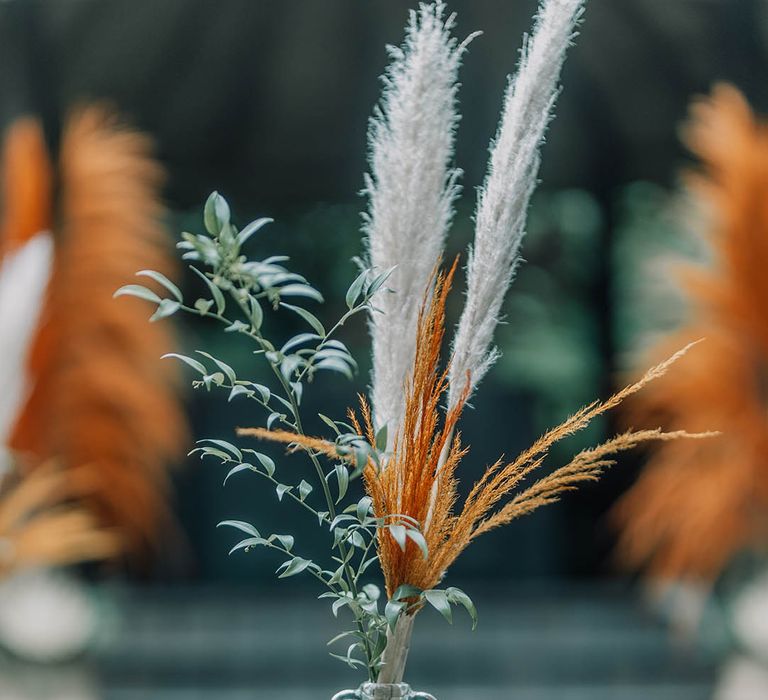 Pampas grass in white and bright orange in mason jar on wooden block