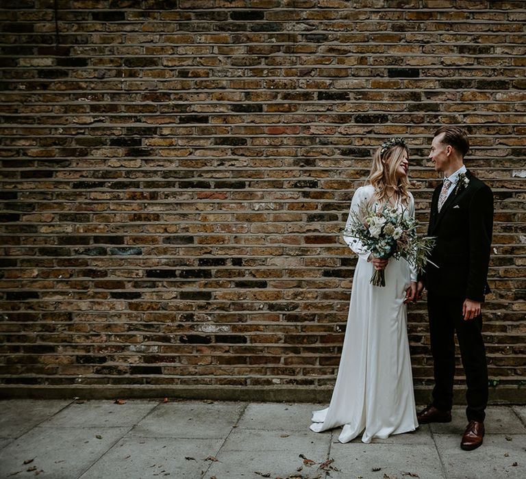 Bride & groom stand in front of brick wall on their wedding day