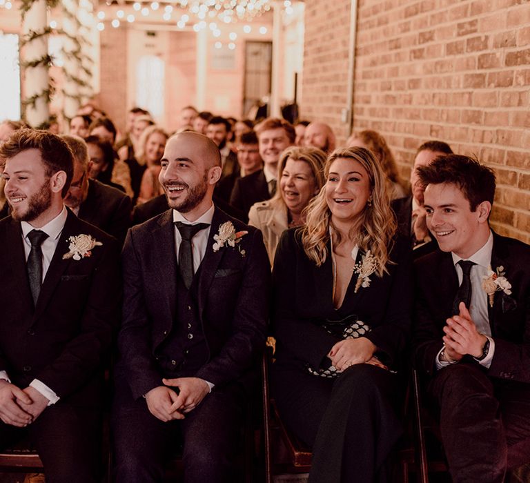 Groomsmen applaud during the wedding ceremony in black tie dress at industrial venue