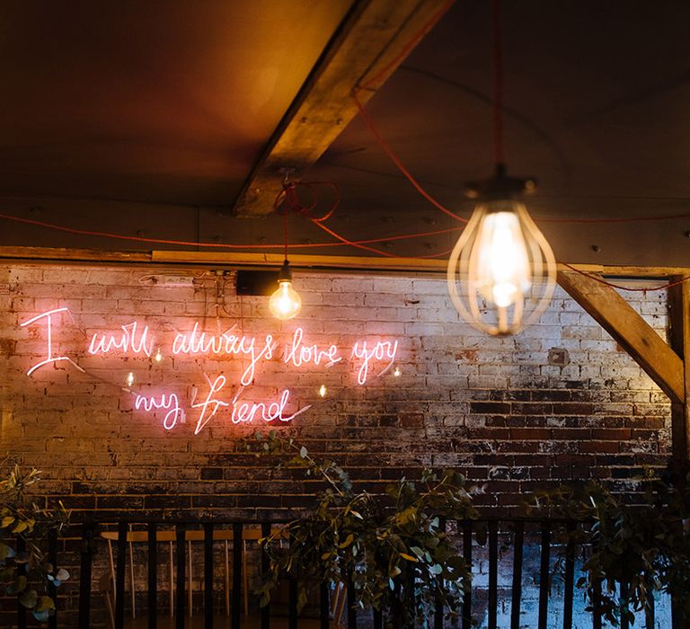 Pink neon sign saying 'I will always love you, my friend' at wedding venue 