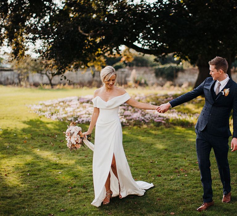 Bride and groom hold hands as they walk the grounds of the wedding venue 