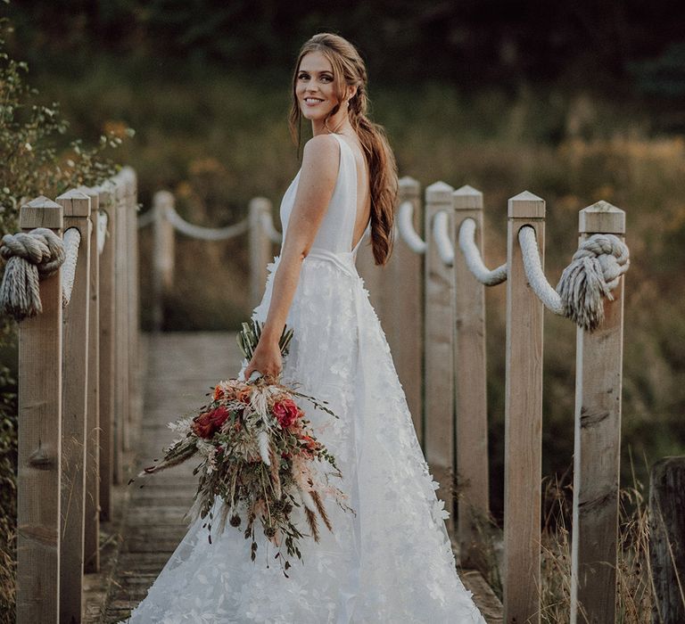 Bride in Savin London lace skirt wedding dress holding autumnal bouquet with intricate ponytail hairstyle