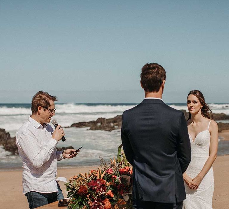 Bride and groom have their wedding ceremony on the beach in South Africa with red and pink tropical flowers 