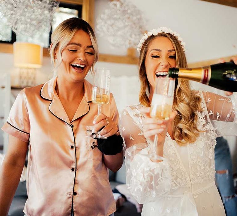 Bride pours herself a drink on the morning of her wedding day with bridesmaid in satin pink pyjamas