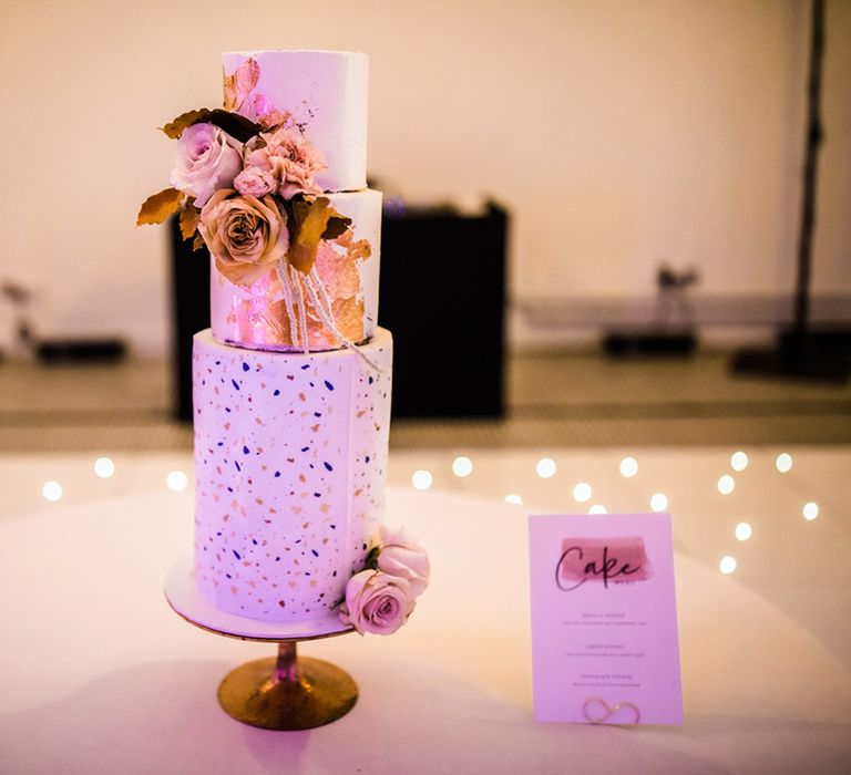 Three tier tall wedding cake with white frosting with gold flakes and flecks with gold and toffee garden roses 