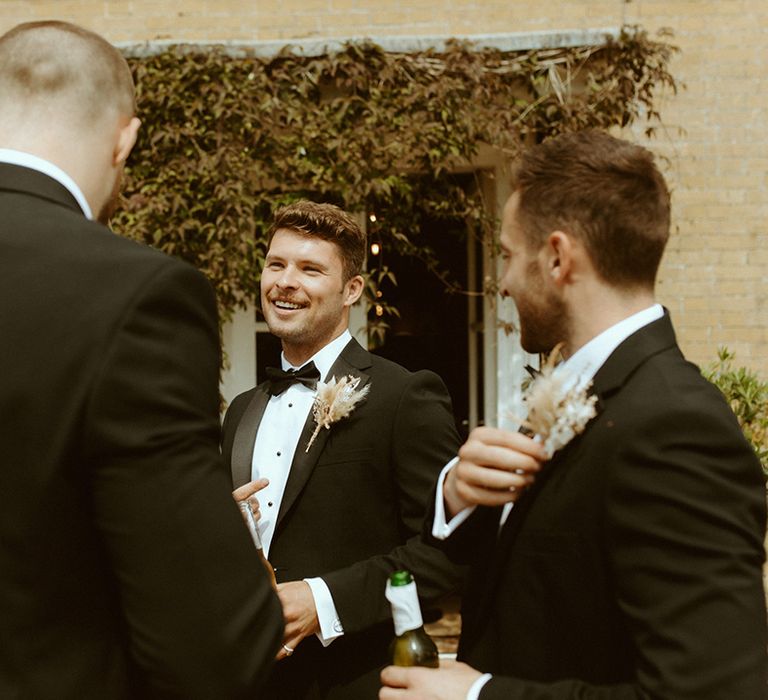 Groomsmen drink beer in black tie with dried flower boutonnières