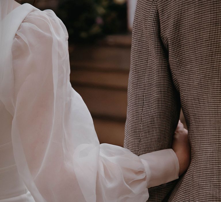 Bride's custom sheer puff sleeves as she links arms with groom in puppytooth suit 