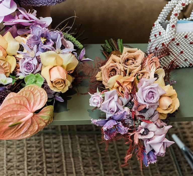 Orange, yellow and purple flower wedding bouquets next to pearl handbag accessory